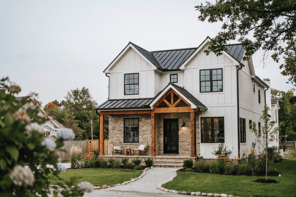 modern farmhouse exterior with chairs on the front porch and flowers to the left in the foreground 
